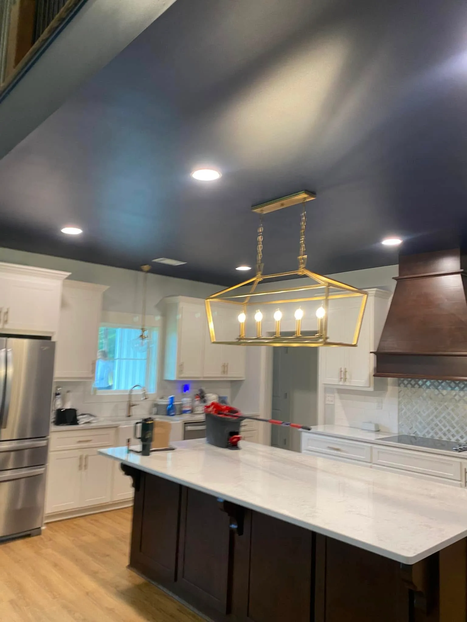 A kitchen with a deep navy ceiling above white cabinets, a dark wood island and range hood, and a gold linear chandelier.