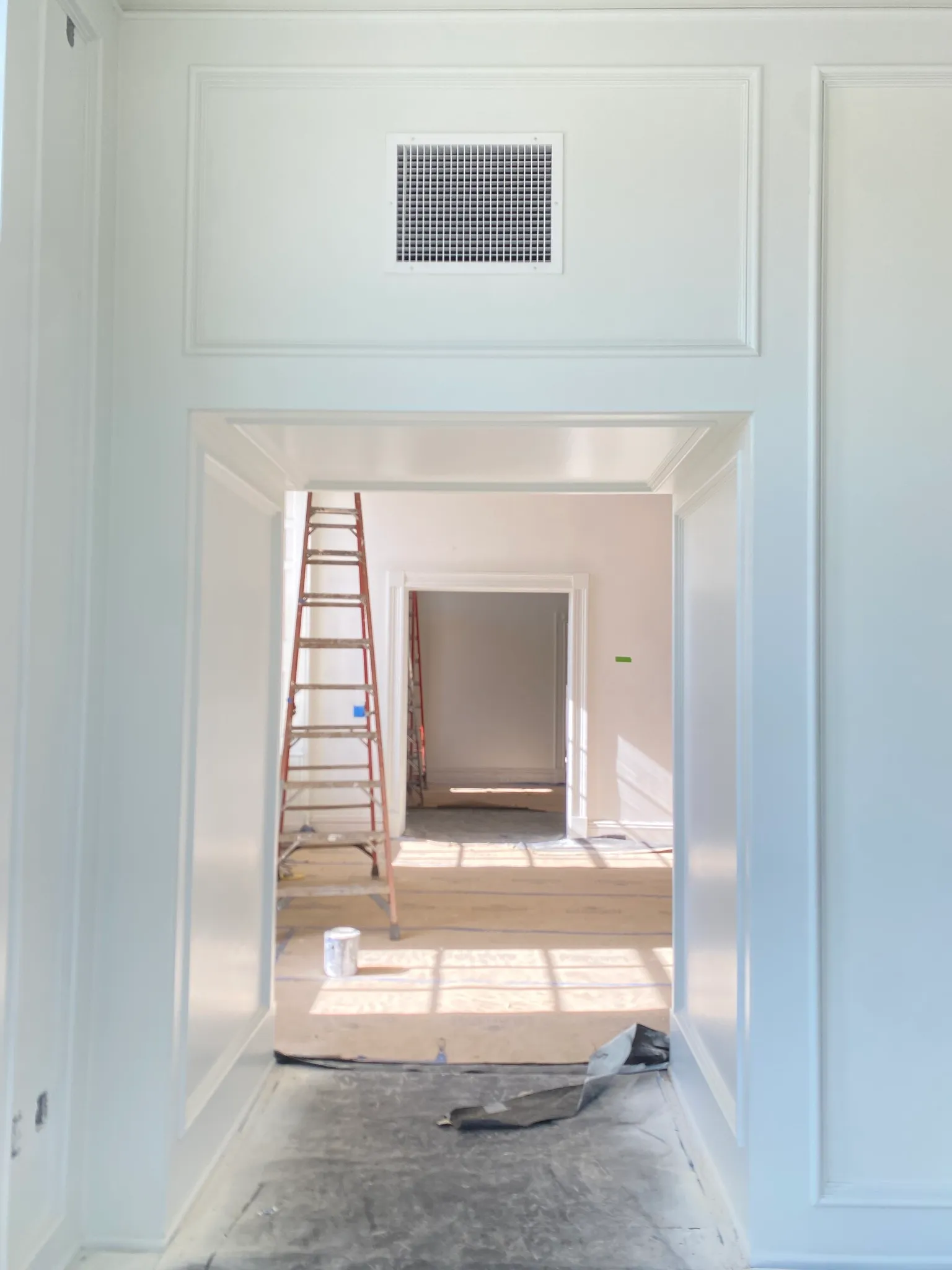 A bright white hallway with paneled wainscoting and crown molding, looking through doorways into rooms still under renovation.